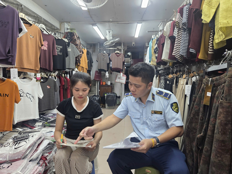 Cán bộ đội Quản lý thị trường số 2 tuyên truyền, vận động hộ kinh doanh trên phố Hàng Đào ký cam kết không kinh doanh hàng giả, hàng hóa xâm phạm quyền sở hữu trí tuệ. Ảnh: Trần Khoa